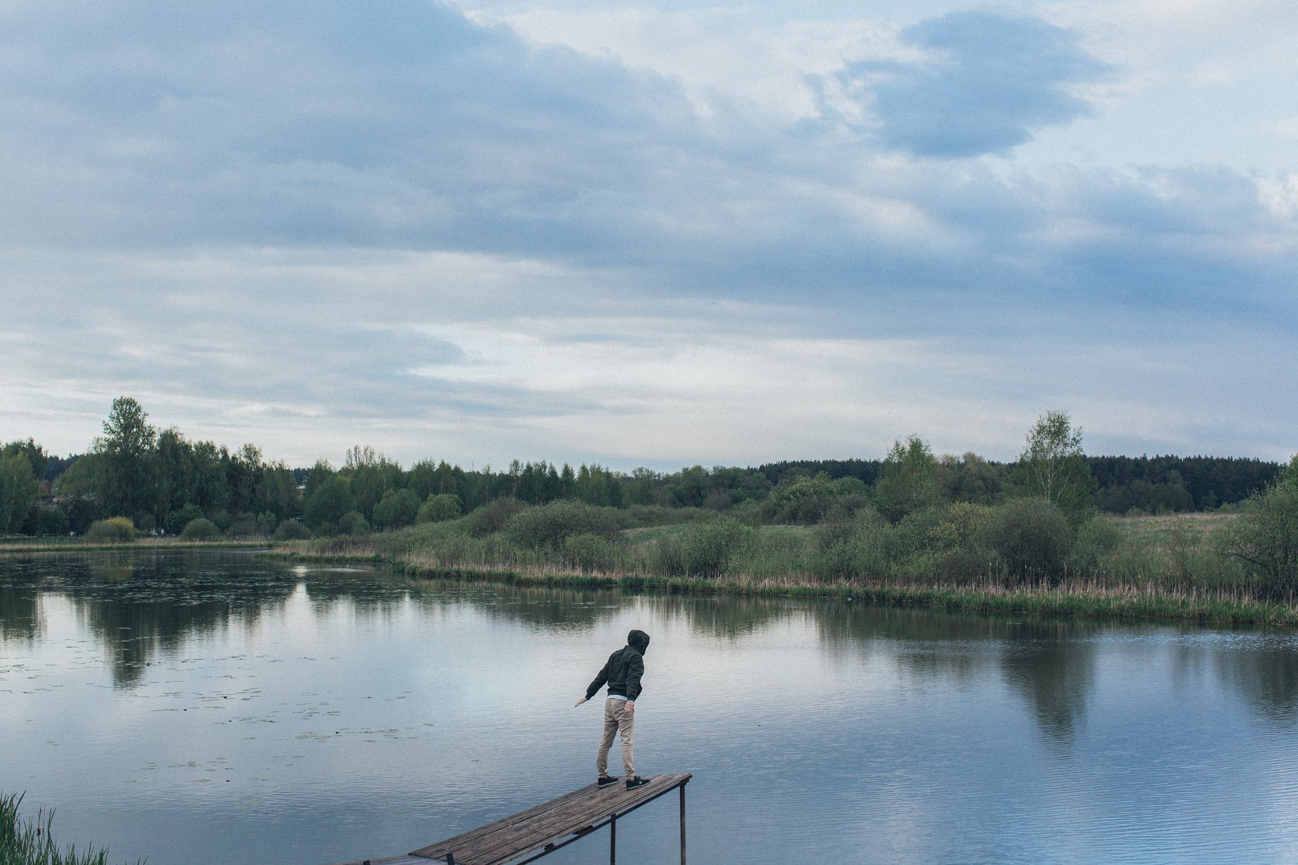man standing on edge of wooden pier near lake